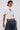 A woman wears the TOO COOL FOR YOU LACEUP BLOUSE, featuring short sleeves, a front keyhole cutout, and puffed details, paired with loose-fitting, low-rise jeans. She completes her look with stylish hoop earrings and short hair.