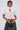 A woman wears the TOO COOL FOR YOU LACEUP BLOUSE—white, high-neck with puffed sleeves, keyhole cutout, and metallic clasps—paired with wide-leg blue jeans, a chain-strap bag, short dark hair, and silver hoop earrings.