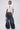 A woman poses against a plain background in the TOO COOL FOR YOU LACEUP BLOUSE, styled with wide-legged blue jeans, a small purse, slicked-back hair, and open-toe shoes.