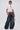 A woman poses against a plain background in the TOO COOL FOR YOU LACEUP BLOUSE—fitted, white with puffed sleeves and keyhole cutout—paired with oversized wide-leg jeans, a silver geometric handbag, and slicked-back wet-look hair.