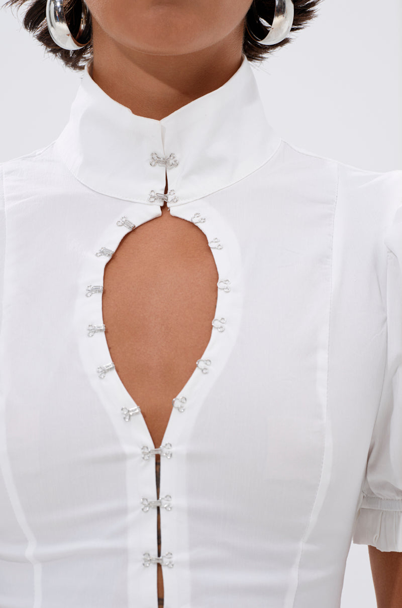 A person wearing the TOO COOL FOR YOU LACEUP BLOUSE, a white top with puffed sleeves, a teardrop-shaped chest cutout, decorative silver clasps, visible seams, and a subtle corset-style design.