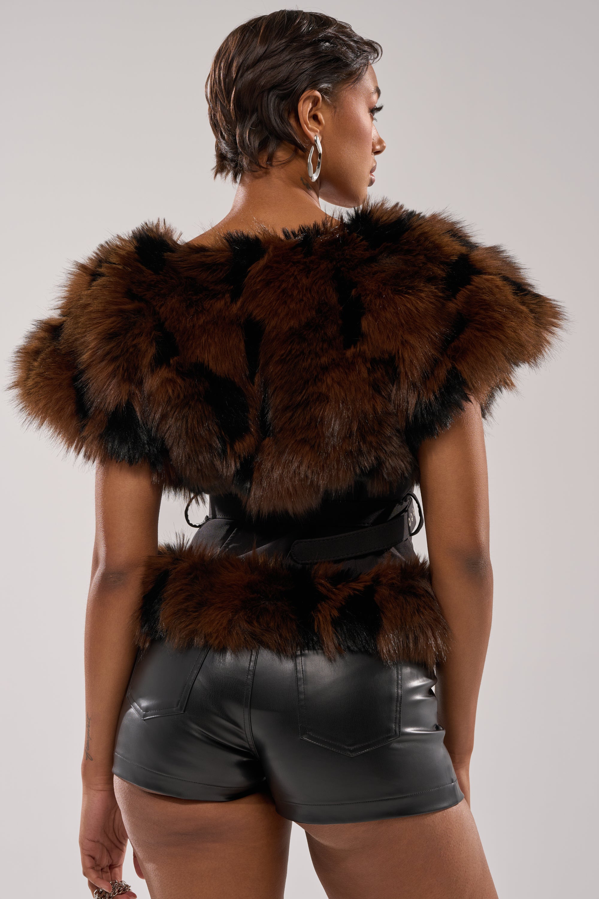 A person with short hair is shown from behind wearing the FEELING WARM FUR BLOUSE in brown and black faux fur, paired with black leather shorts, standing against a plain background. 4