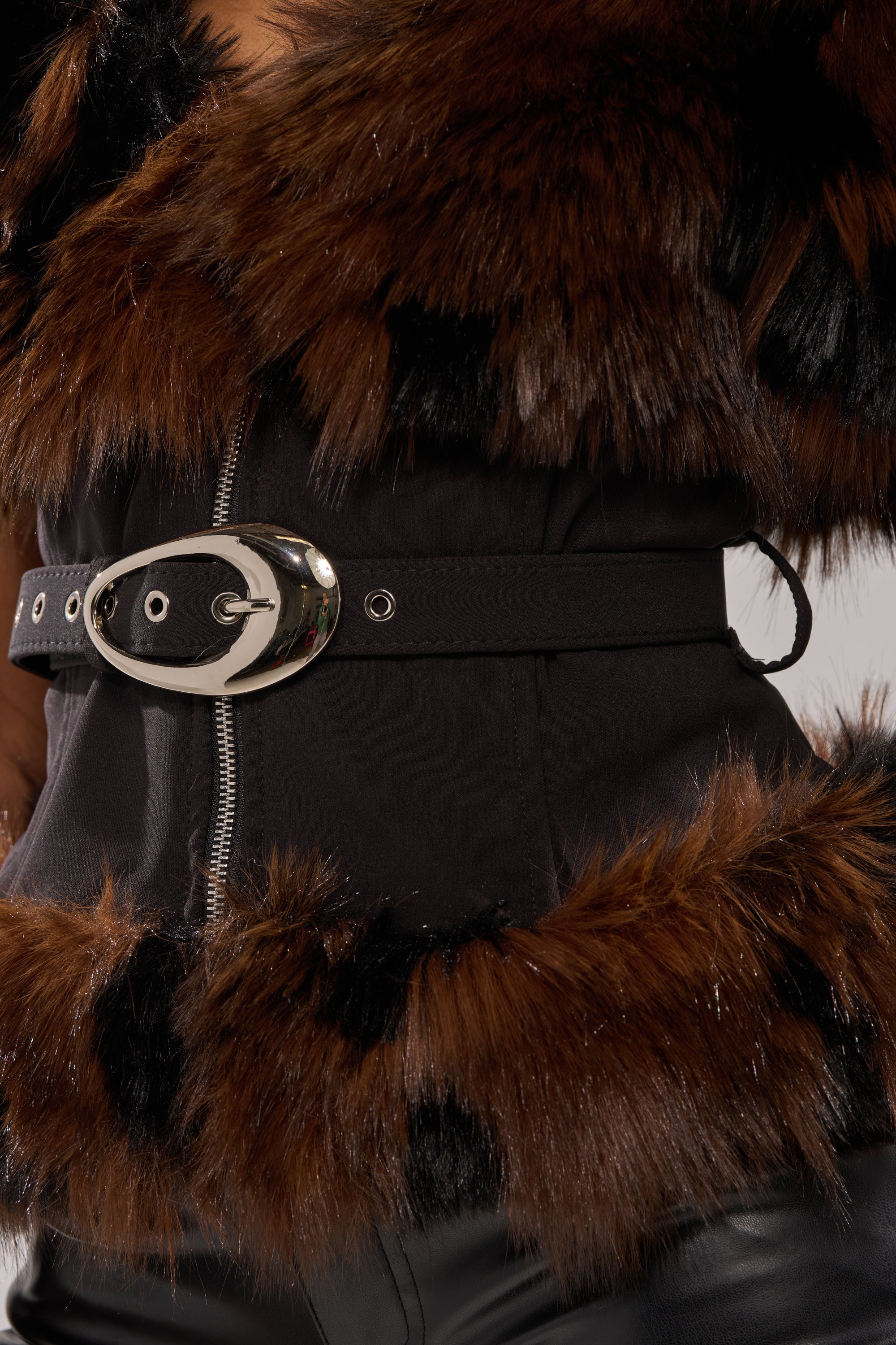 A close-up of a person in winter-chic style, wearing the FEELING WARM FUR BLOUSE with faux fur trim, metallic adjustable belt buckle, black fabric, brown fur accents, and paired with sleek black leather pants. 7