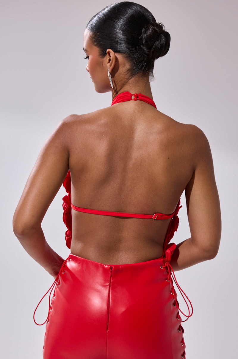 Woman with hair in a sleek bun, wearing the GIVE ME A ROSE BODYSUIT featuring a shiny red skirt and deep plunge halter neckline, shown from the back against a simple light gray background. 3