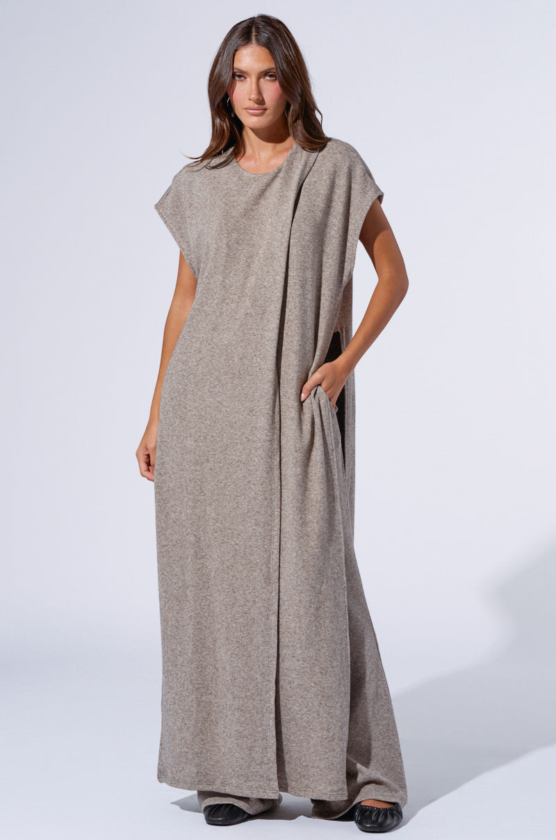 A woman stands wearing the VIBE OUT FLARE LEG KNIT PANT IN GREY with a high-rise relaxed fit. She has her right hand in the pant pocket and is looking directly at the camera. The background is a plain light gray, and she is wearing black shoes. 7