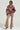 A woman poses confidently, wearing a stylish WILD SIDE MIXED MEDIA SWEATSHIRT featuring a red and zebra pattern, paired with beige flared pants and sparkling heels. She accessorizes with layered gold necklaces.