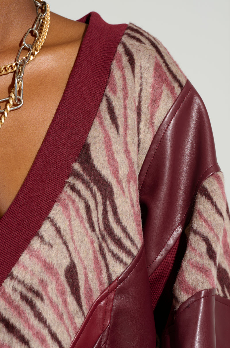 A close-up features someone wearing the WILD SIDE MIXED MEDIA SWEATSHIRT in maroon and beige, adorned with maroon leather patches. The look is complemented by a gold chain necklace, highlighting the intricate details of the clothing.