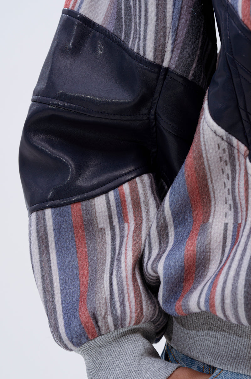 A close-up of a person's arm in the INTO THE WILD DEEP V SWEATSHIRT, featuring black faux leather chevron patches, multi-colored stripes in gray, blue, and red, and light gray ribbed cuffs.