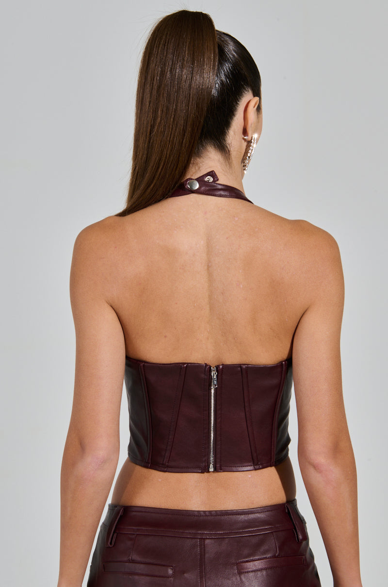 A person with long, straight hair in a high ponytail is facing away from the camera, wearing the Temptation's Best Friend Corset in burgundy with a visible back zipper, paired with matching leather pants for a western-inspired look.