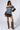 A Y2K baddie wears a stylish off-the-shoulder stretchy blue denim top with fur trim, paired with the FRANCESCA FUR TRIM DENIM MINI SKIRT and knee-high snake print boots. With long dark hair and sunglasses, she poses confidently against a plain background.