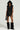 A person exudes confidence and style in a black ensemble that includes the DELANEY FUR TRIM MINI SKIRT. They complete their bold look with a hooded vest featuring cargo-style pockets, large sunglasses, furry boots, and a small bag against a simple backdrop.