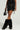 A person in the DELANEY FUR TRIM MINI SKIRT with metal eyelets, styled with matching black fur boots and a small black handbag, standing against a plain, light-colored background.