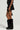 A person wearing a black fur vest, the DELANEY FUR TRIM MINI SKIRT, and tall black boots stands against a neutral background. The outfit is accessorized with a studded belt and a small black bag, adding an edgy flair to the ensemble.