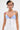 A person with short dark hair and tattoos wears the KLYA CORSET—a strapless, structured white and blue striped top with decorative buttons—adding Nautical Edge as they stand against a plain light background.