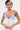 A person with short, dark hair and a blonde streak wears the strapless KLYA CORSET in white and blue with decorative buttons. Tattoos, facial piercings, and large hoop earrings add edge to their structured, seductive look.