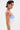 A person with short dark hair and silver earrings models the KLYA CORSET, a strapless colorblock piece in white and light blue. Pink makeup drips across their shoulder as they pose sideways, confidently facing the camera.