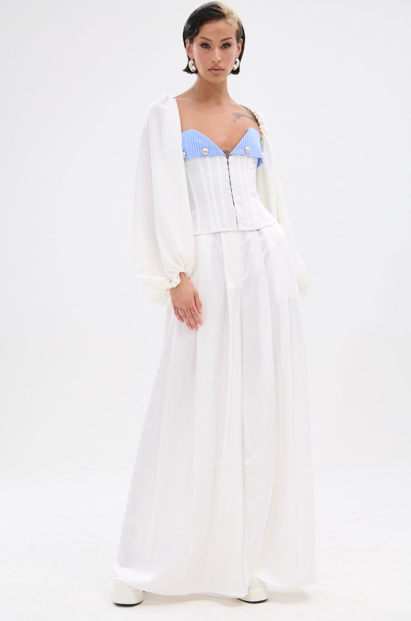 A woman poses against a white background in a long white skirt, loose jacket, and KLYA CORSET—a blue and white striped colorblock piece with nautical flair—styled with slicked-back hair and white platform shoes.