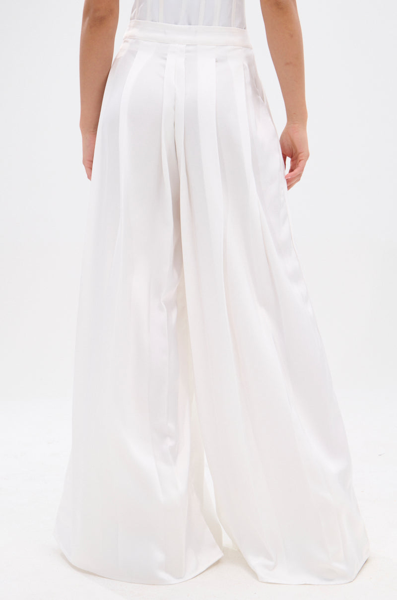 A person models the KYLA TROUSER, featuring a high-rise silhouette and wide-leg white satin with vertical stripes, viewed from the back against a plain white background. 4