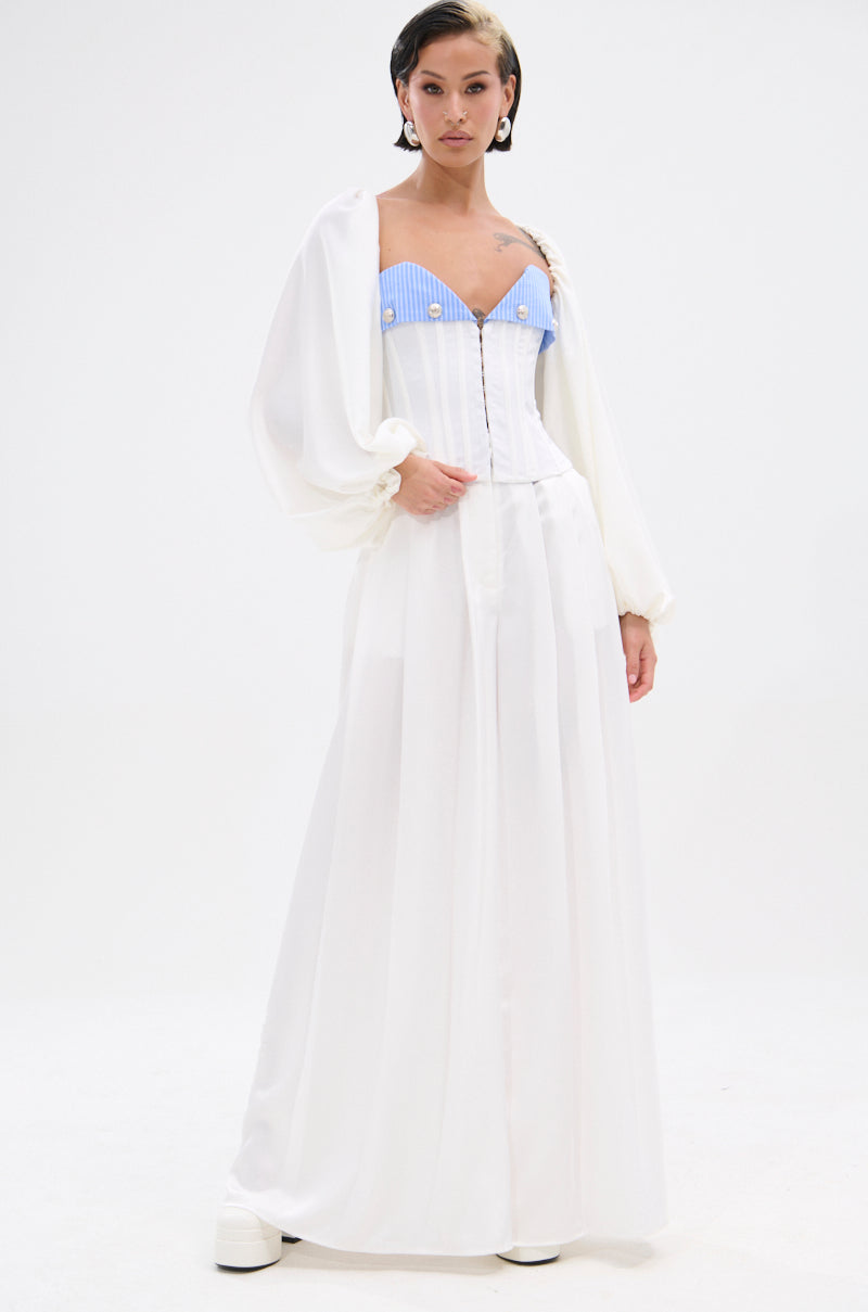 A person stands against a white background wearing the KYLA TROUSER—wide-leg satin pants—paired with an off-white open blouse over a light blue and white striped corset top, short slicked-back hair, and white platform shoes. 5