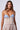 A woman with long, wavy hair models the "TAKE IT EASY CORSET TOP," which is strapless and features a light blue and white pinstripe neckline with buttons and a beige lower section enhanced by boning. She gazes directly at the camera against a plain, light background.