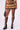 A person is modeling a fashion-forward outfit, showcasing the DRIVE ME WILD FUR MINI SKIRT made of layered ombre faux fur in mixed brown and orange colors. Paired with the skirt are knee-high black boots featuring multiple buckles, and the person is holding a chic black handbag.