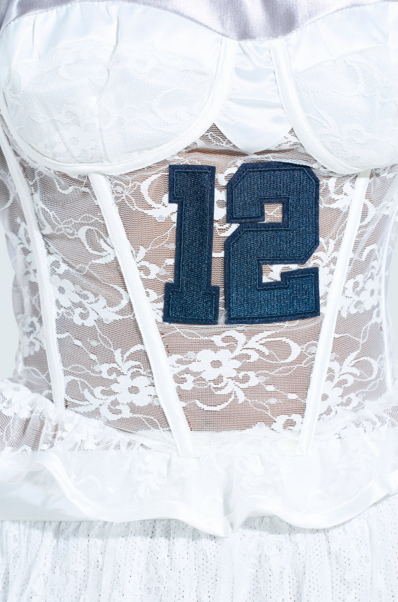 Close-up of a white lace corset featuring sporty accent stripes and a large blue number "12" patch on the back. The corset boasts floral lace patterns and sheer sections, resembling the Lucky Me Jersey.