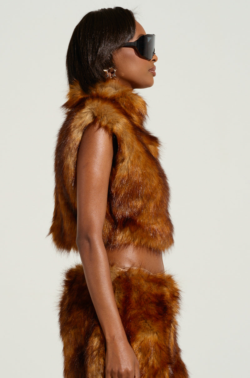 A person wearing fashionable sunglasses and a WILD CHILD CROPPED FUR VEST, combined with a brown fur-inspired sleeveless top and skirt, poses in profile against a simple backdrop.