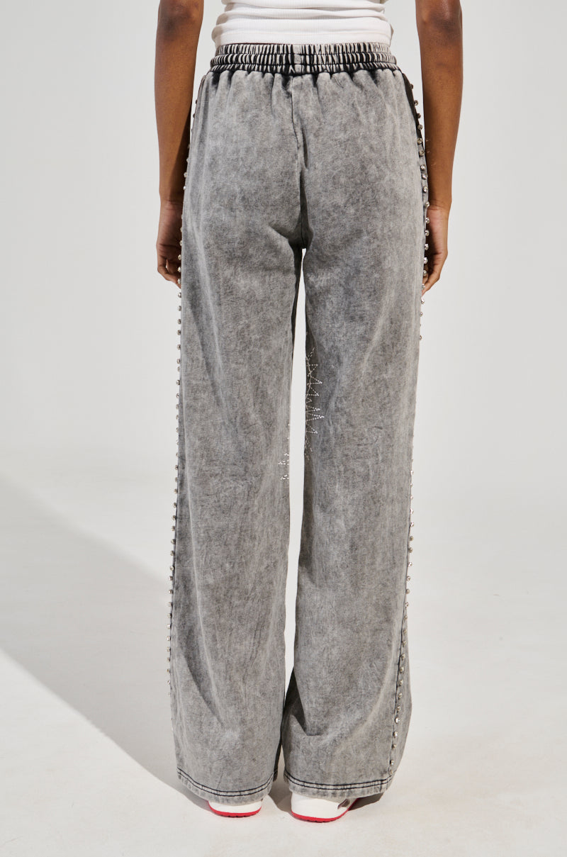 Rear view of a person in WINNERS CLUB WIDE LEG JOGGER, made from cotton knit with a gathered waistband. White shoes with red accents are visible below, against a plain background, radiating effortless style.
