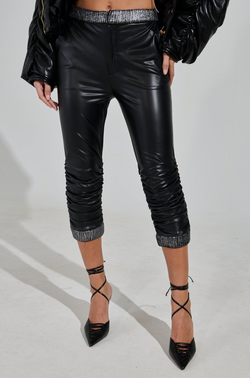 Someone is wearing the "Always Best Dressed Capri in Black PU" with ruched detailing and sparkly cuffs, paired with black strappy high heels against a plain light-colored background. 1