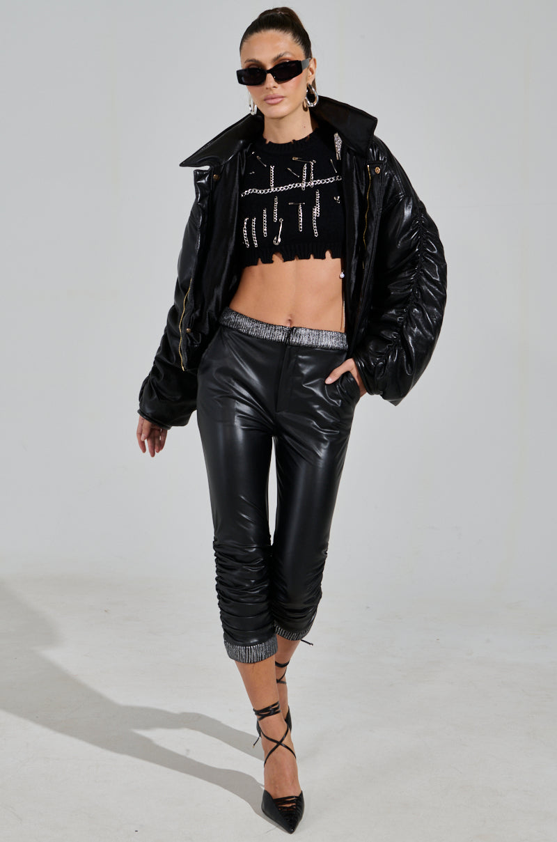 Dressed in the chic ALWAYS BEST DRESSED CAPRI IN BLACK PU, they're styled with a black faux leather jacket and pants, fringe-detailed black crop top, stylish sunglasses, and sleek heels. Posing confidently against a plain background showcases their high rise fashion sensibilities. 6