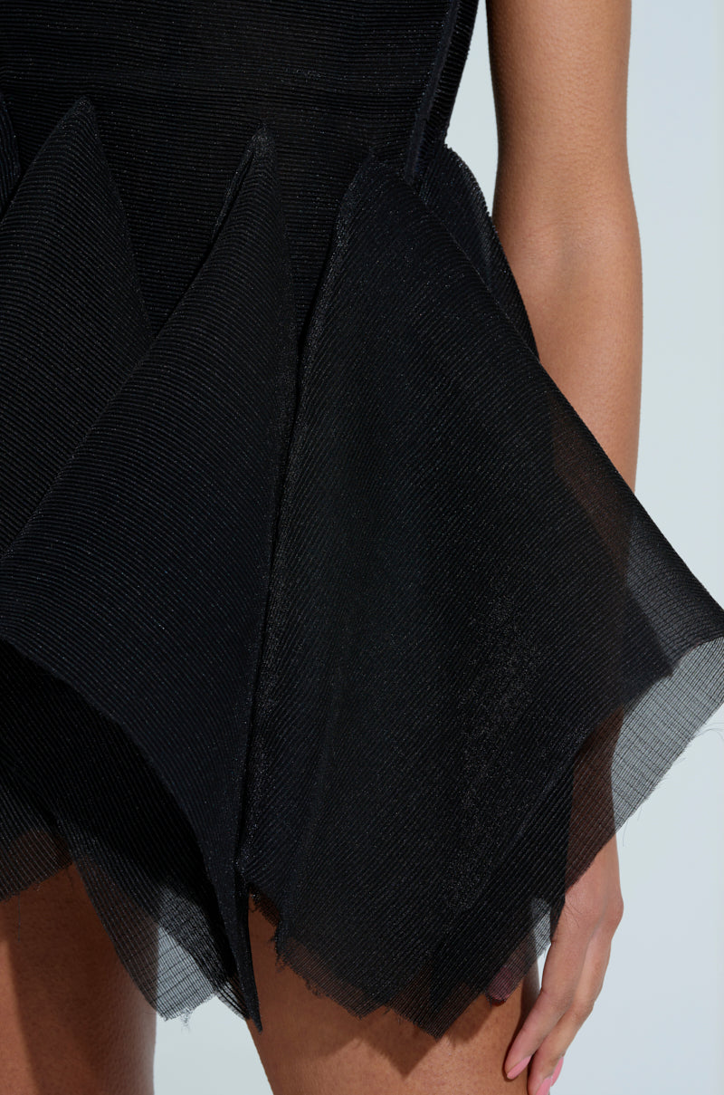 A close-up of the avant-garde CRAZY 4 YOU BLOUSE with structured, angular fabric panels and a strapless sweetheart neckline. The textured surface adds intrigue as a person partially reveals their arm on the right against a pale blue background.