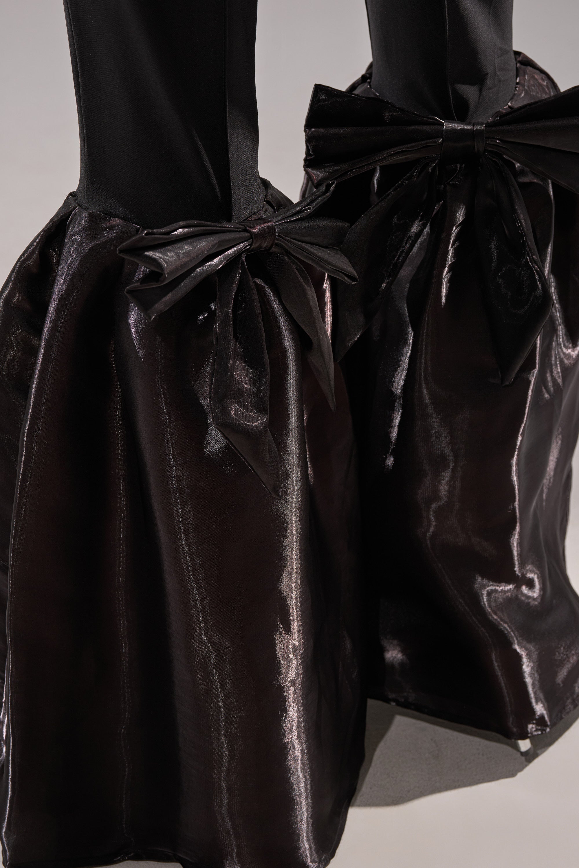 Close-up of the LILY TROUSER WITH BOW IN BLACK, featuring voluminous satin pants with large matching bows tied at the ankles, creating a sculptural effect against a neutral background.