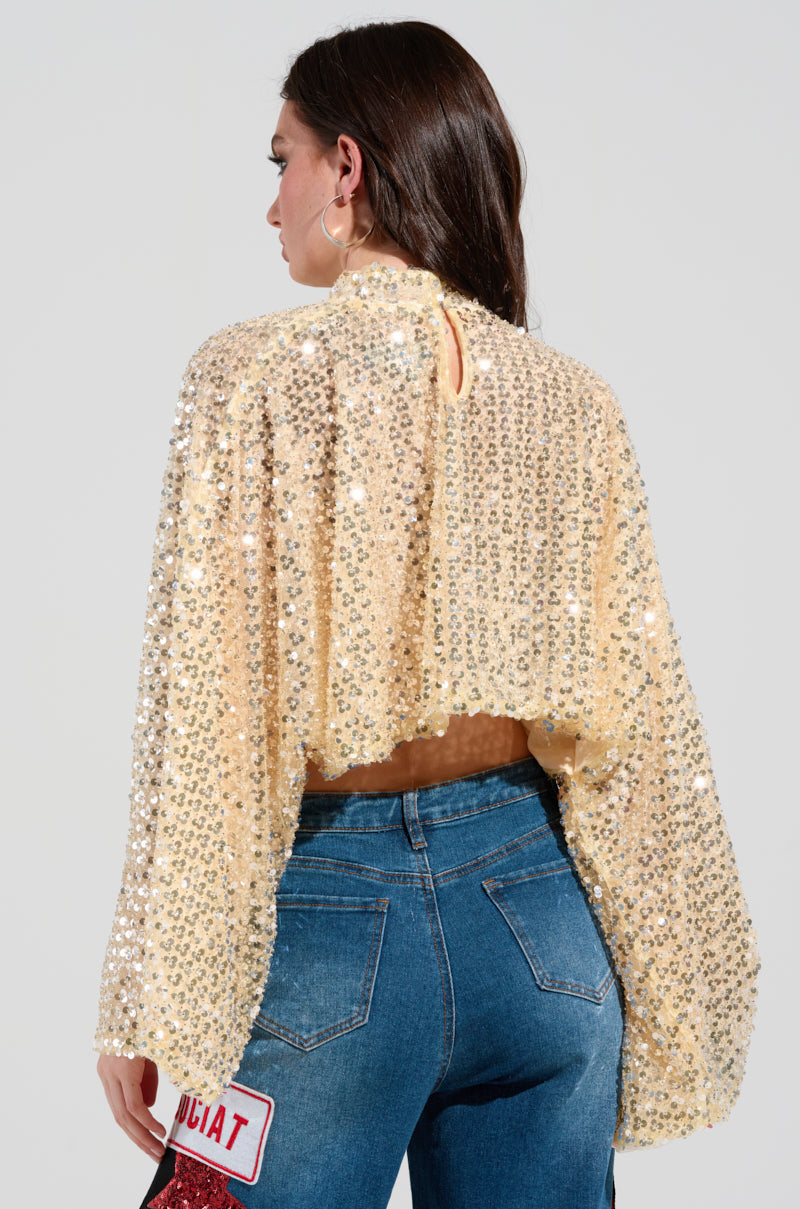 A person with long, dark hair is wearing a SLYLINE Sequin Blouse paired with blue jeans. They are facing away, allowing the detailed texture of the top to catch the light, making it perfect for a holiday party look. A patch with "EXPLICIT" decorates the back of the jeans.