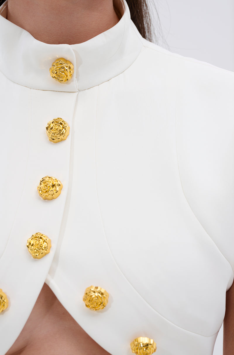 Close-up of the THINK ABOUT ME SLEEVELESS BLOUSE IN WHITE, a structured and elegant blouse with a high collar and dual rows of metallic gold rose-shaped buttons. 6