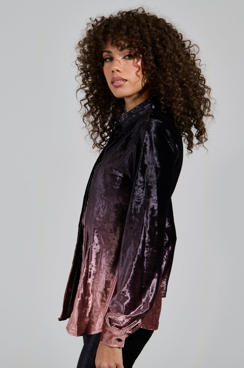 A person with curly hair wearing a NEVER SWITCH UP OMBRE BUTTON DOWN BLOUSE IN BLACK, which transitions from dark purple to deep pink, stands in profile against a plain background, effortlessly capturing the spirit of a holiday ensemble.