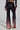 A person dressed in a fashionable ensemble featuring the NEVER SWITCH UP OMBRE FLARE LEG PANT IN BLACK, showcasing a chic high-rise design with crushed velvet material that elegantly transitions from dark brown at the top to light pink at the bottom, complemented by a matching velvet top against a plain backdrop.