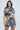 Wearing a captivating COUNTDOWN TO MIDNIGHT TOP, adorned with dazzling reflective discs and sequins, a person poses against a neutral background. The cropped top and skirt ensemble complements their confident expression and long brown hair, creating an enchanting look.