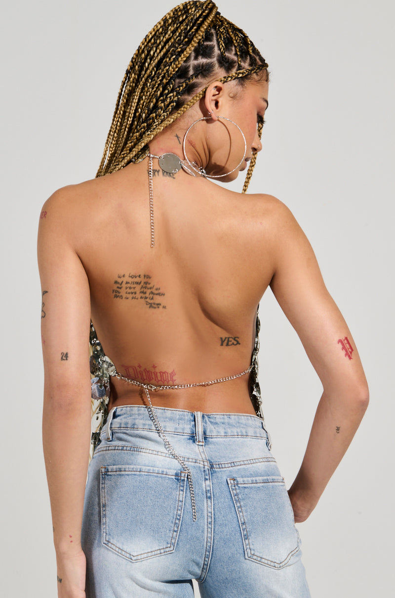 A person with braided hair is facing away, donning large hoop earrings and the PARTY ALL NIGHT SEQUIN HALTER NECK TOP, which is paired with light blue jeans. Various tattoos adorn their back and arms against a neutral gray background. 4