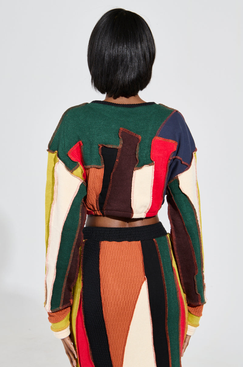 A person with short black hair is facing away, wearing the BEAST MODE SWEATER, which boasts a cropped silhouette and a colorful patchwork design. The sweater features vertical abstract patterns in shades of green, red, orange, brown, and cream against a plain white background. 4