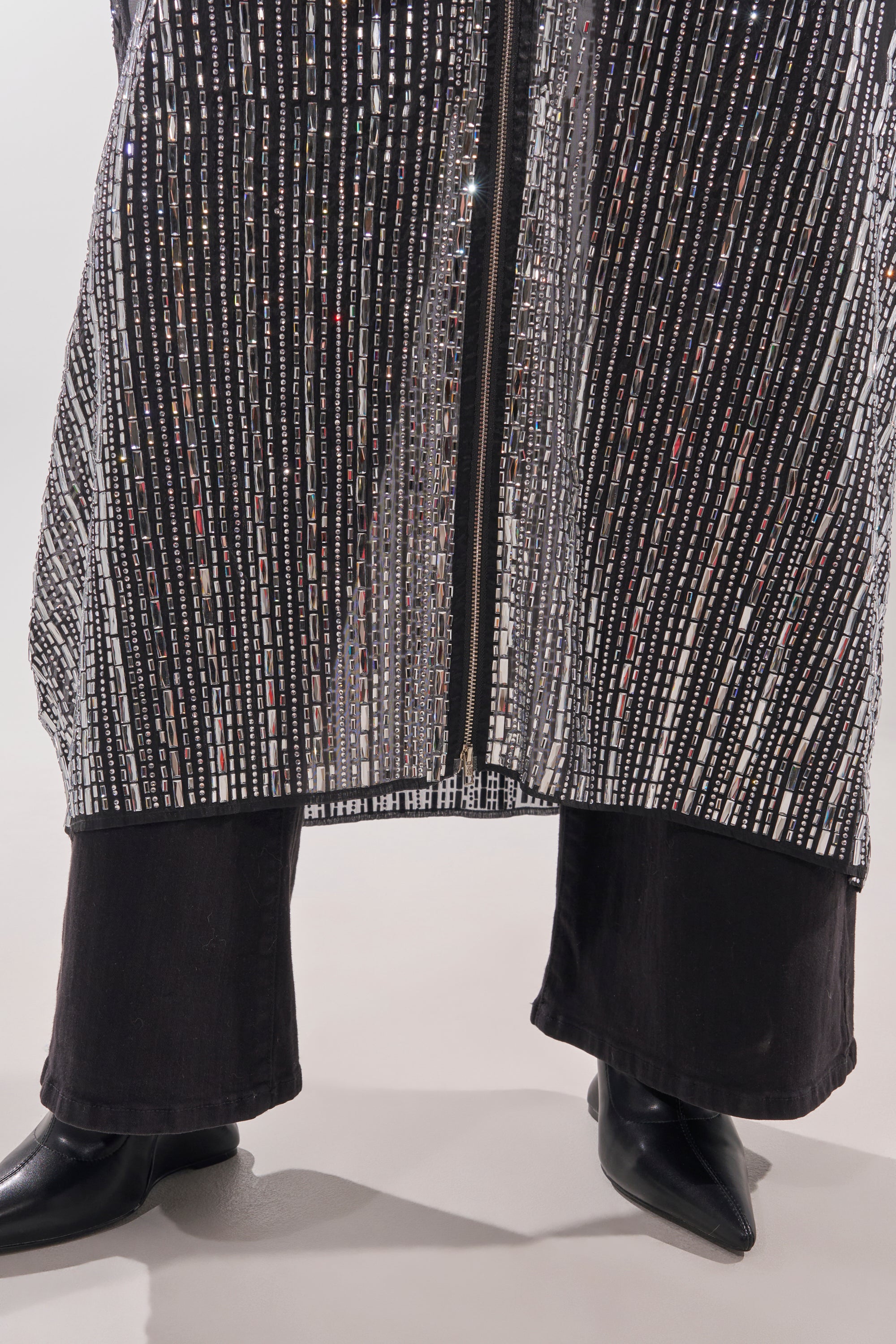A person stands with legs apart wearing flared black pants, pointed black shoes, and the SPARKLE AND SHINE BLOUSE—a sheer overlay adorned with vertical rows of sequins. 9
