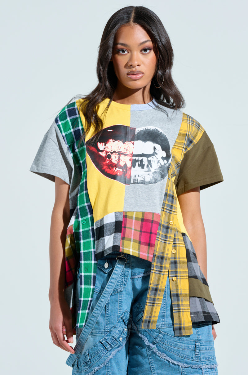A woman wears a REBUILT OVERSIZED FLANNEL T-SHIRT with plaid and a smiling mouth graphic, paired with blue patterned jeans, against a plain light gray backdrop.