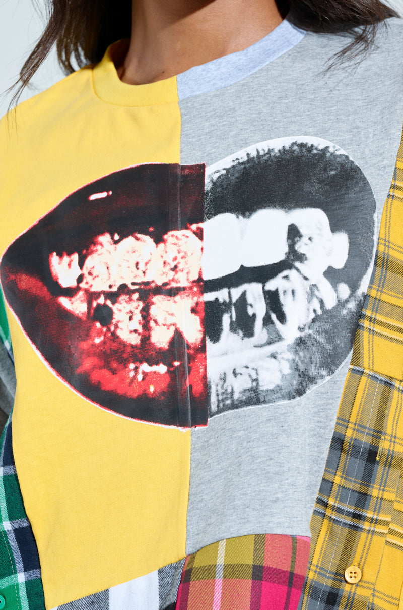 A close-up of someone in the REBUILT OVERSIZED FLANNEL T-SHIRT, showcasing a bold patchwork with a large smiling mouth graphic. The shirt blends plaid patterns in yellow, green, and red across different sections.