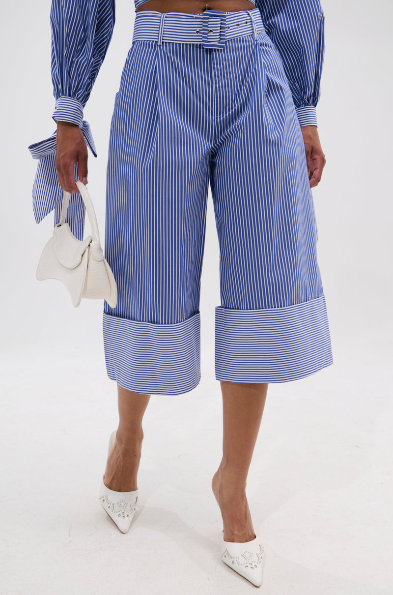 A woman wears the UNDER THE SUN STRIPE SHORT with a matching top, white pointed-toe shoes, and a small white handbag, creating a chic summer look against a plain white background.