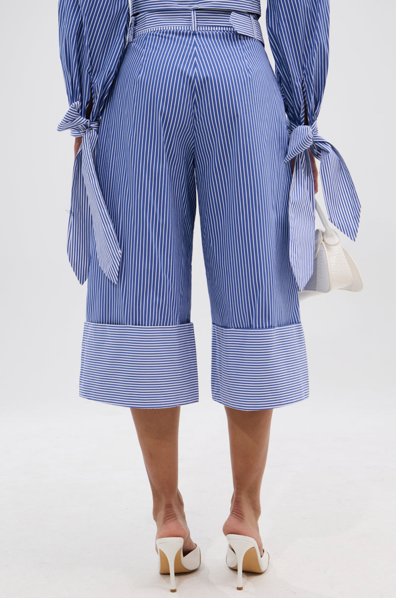 Wearing the UNDER THE SUN STRIPE SHORT and a matching long-sleeve top with tied cuffs, this person pairs white high heels with a small white handbag, all viewed from the back.