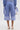 Wearing the UNDER THE SUN STRIPE SHORT and a matching long-sleeve top with tied cuffs, this person pairs white high heels with a small white handbag, all viewed from the back.