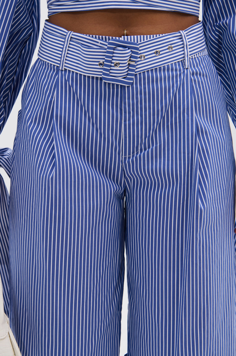 A close-up shows a person wearing UNDER THE SUN STRIPE SHORTS—high-waisted, blue-and-white striped with a matching belt, buttons, belt loops, and a waistband. The shirt also matches the UNDER THE SUN STRIPE SHORT pattern.