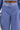 A close-up shows a person wearing UNDER THE SUN STRIPE SHORTS—high-waisted, blue-and-white striped with a matching belt, buttons, belt loops, and a waistband. The shirt also matches the UNDER THE SUN STRIPE SHORT pattern.