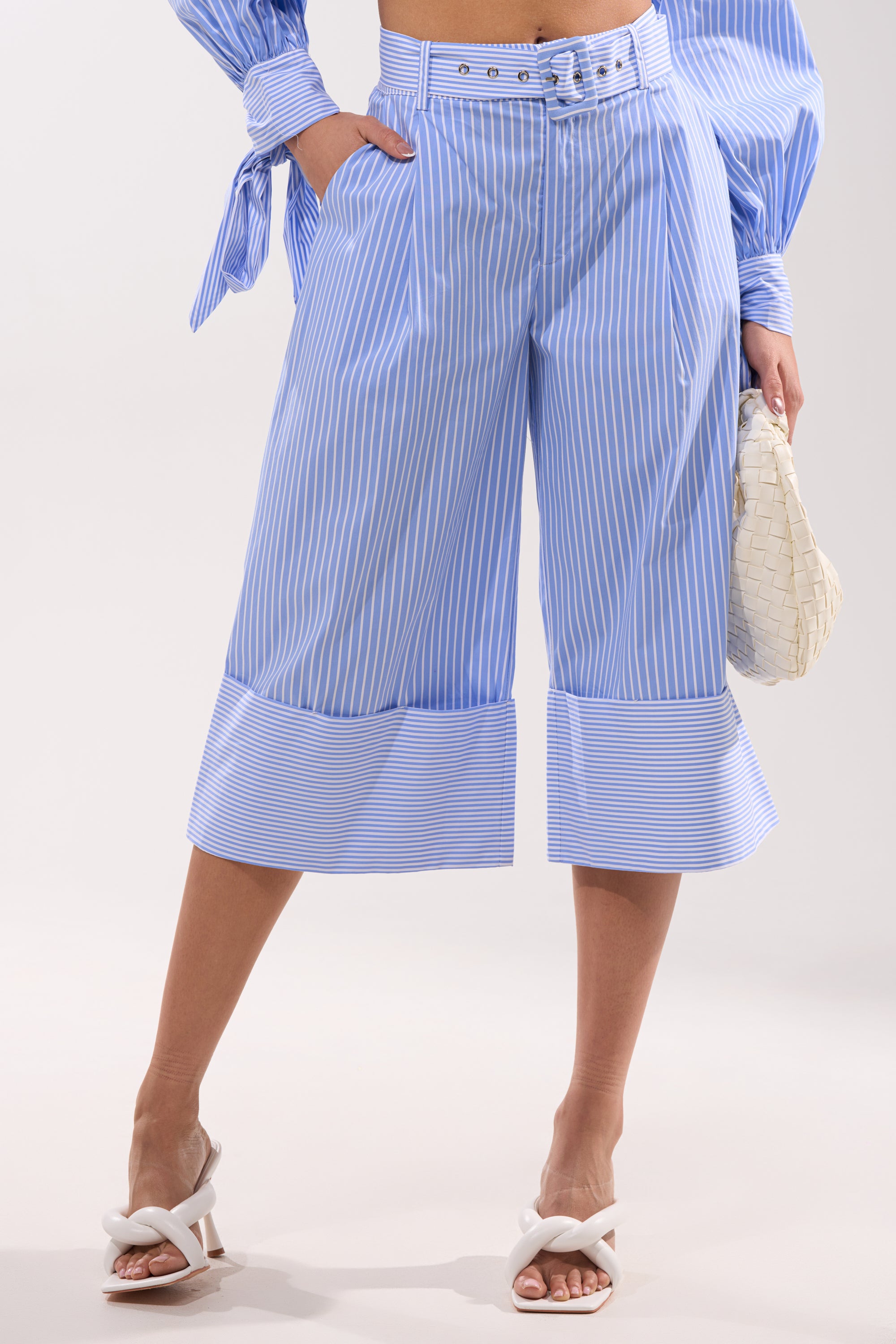 Wearing the NOT LIKE ANYONE ELSE POPLIN SHORT, a matching blouse, white heeled sandals, and holding a woven white clutch bag.