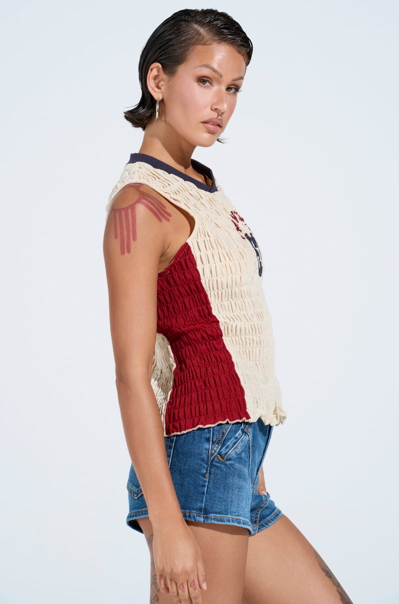 A woman with short, slicked-back hair wears the ADDICTED RUCHED JERSEY TOP and denim shorts, standing in profile against a light background that accentuates a geometric tattoo on her upper arm.