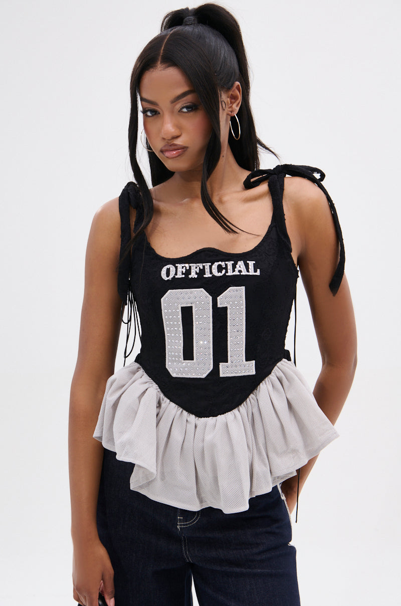 A woman wearing the OFFICIAL PRINCESS LACE PEPLUM CORSET TOP, featuring “OFFICIAL 01” on the front and a mesh peplum hem, stands against a white background and looks confidently at the camera.